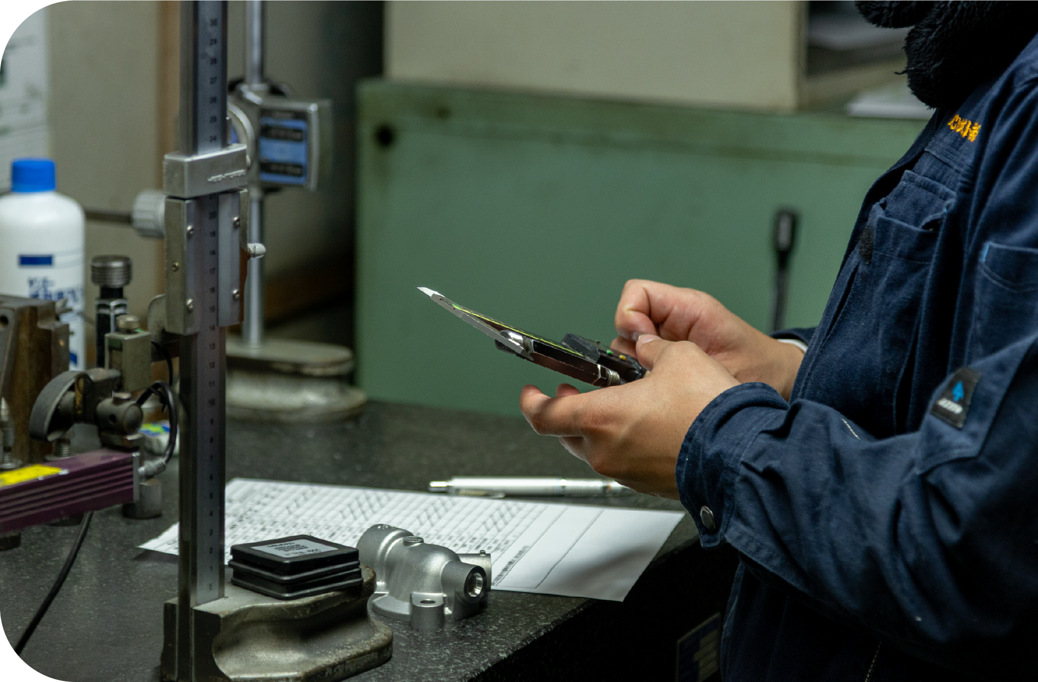 Worker inspecting a metal part with calipers at a quality control workstation.