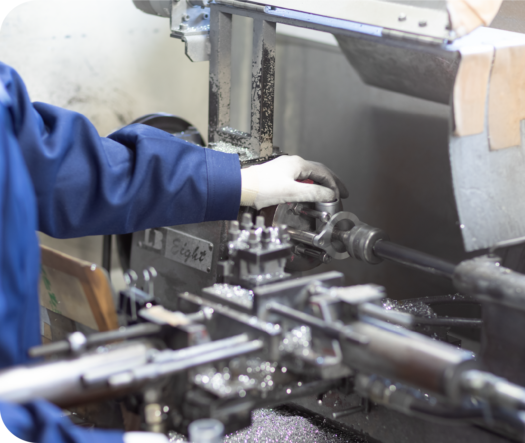 Worker in blue uniform operating a metal lathe machine in a factory.