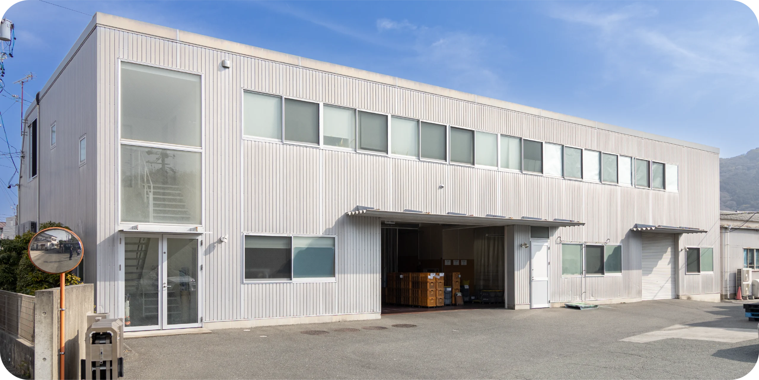Exterior of a two-story industrial building with a loading bay and mountains in the background.